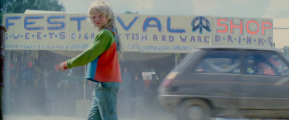 A child walking past the Festival Shop sign, a frame from Glastonbury The Movie